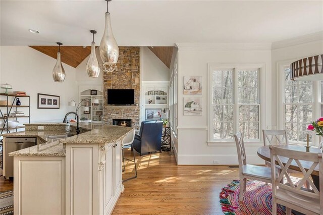kitchen featuring a sink, a fireplace, light wood-style flooring, decorative light fixtures, and stainless steel dishwasher