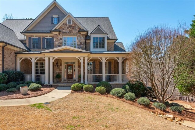 craftsman inspired home featuring a porch, a front lawn, and stone siding