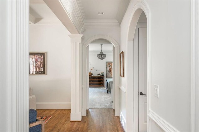 hallway with baseboards, ornamental molding, arched walkways, and wood finished floors