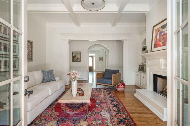 living room featuring arched walkways, ornamental molding, coffered ceiling, and wood finished floors