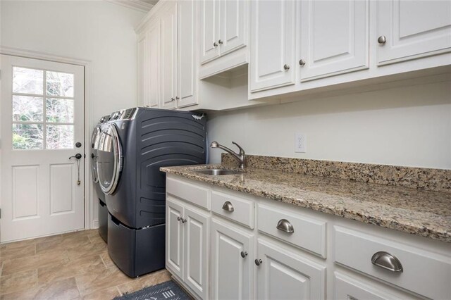 laundry room featuring a sink, stone finish floor, washing machine and dryer, and cabinet space