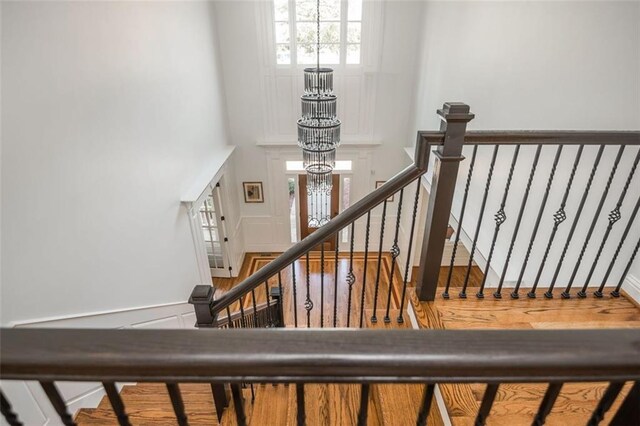 stairway with a towering ceiling, wood finished floors, and a notable chandelier