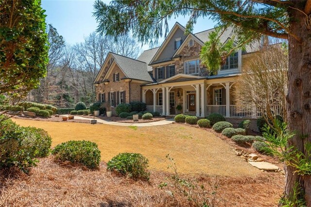 back of property featuring covered porch, a yard, and stone siding