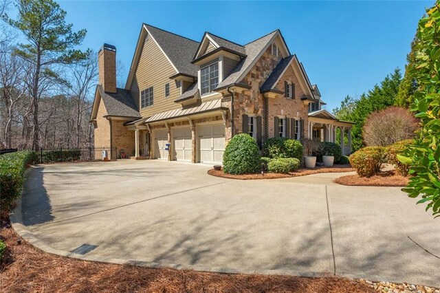 view of front of property featuring driveway, a chimney, fence, an attached garage, and stone siding