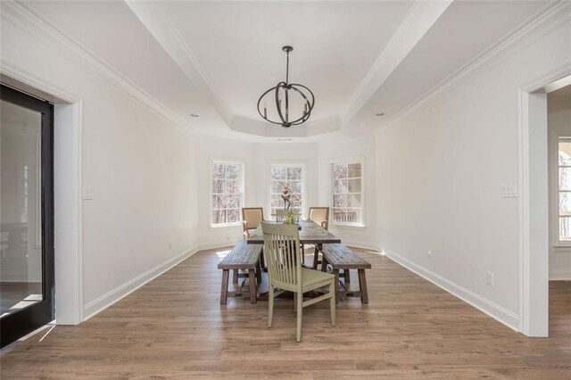 dining space featuring wood finished floors, a raised ceiling, baseboards, a notable chandelier, and ornamental molding