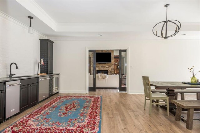 kitchen featuring a notable chandelier, a sink, a raised ceiling, dishwasher, and a stone fireplace