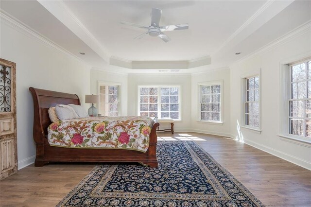 bedroom with ceiling fan, wood finished floors, baseboards, ornamental molding, and a tray ceiling