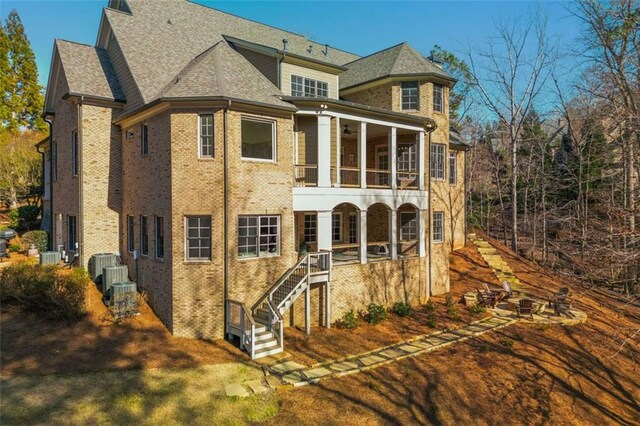 back of property with stairway, brick siding, a balcony, and roof with shingles