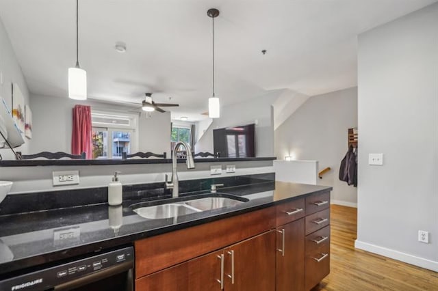 kitchen featuring light hardwood / wood-style flooring, pendant lighting, dishwasher, sink, and dark stone countertops