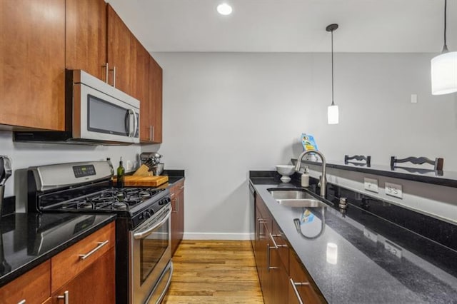 kitchen featuring light hardwood / wood-style floors, appliances with stainless steel finishes, sink, decorative light fixtures, and dark stone counters