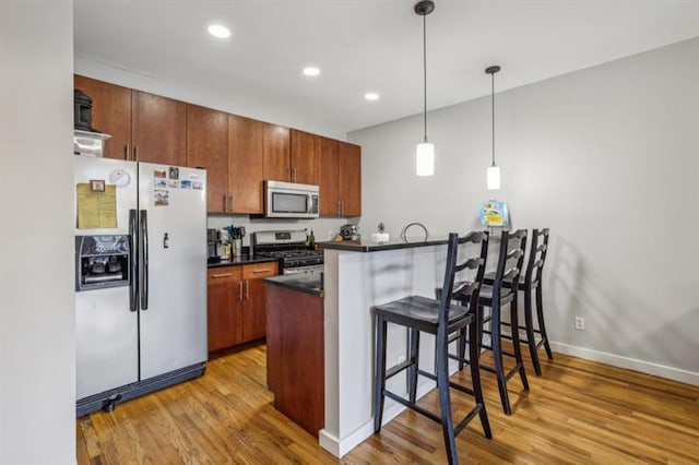 kitchen featuring pendant lighting, light hardwood / wood-style flooring, kitchen peninsula, and appliances with stainless steel finishes