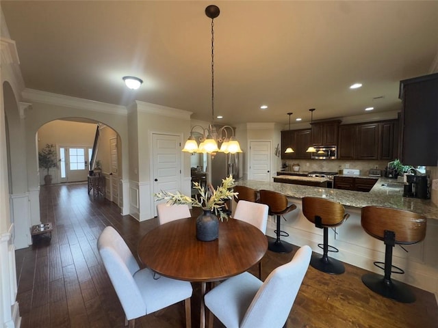 dining space with arched walkways, wainscoting, crown molding, and dark wood-type flooring