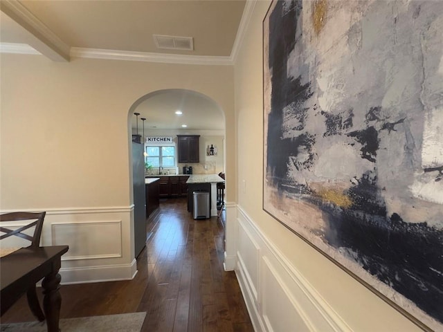 corridor with visible vents, dark wood finished floors, arched walkways, wainscoting, and crown molding