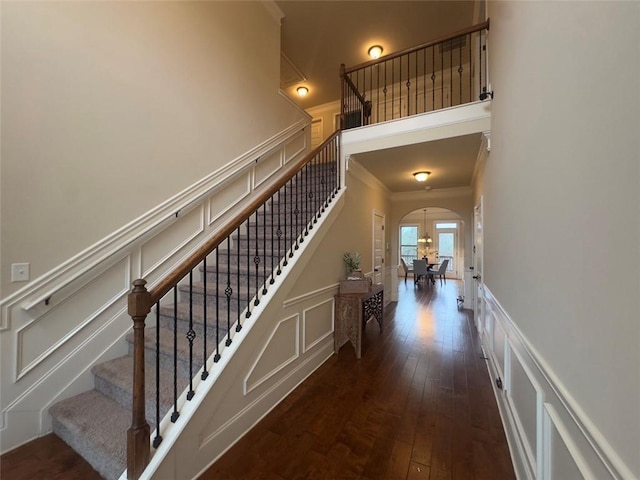 stairs with arched walkways, a decorative wall, ornamental molding, and hardwood / wood-style flooring