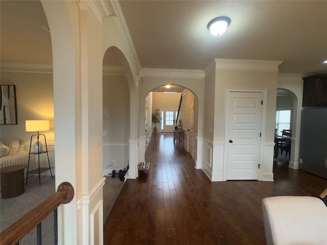 corridor with a wainscoted wall, dark wood-type flooring, crown molding, and arched walkways