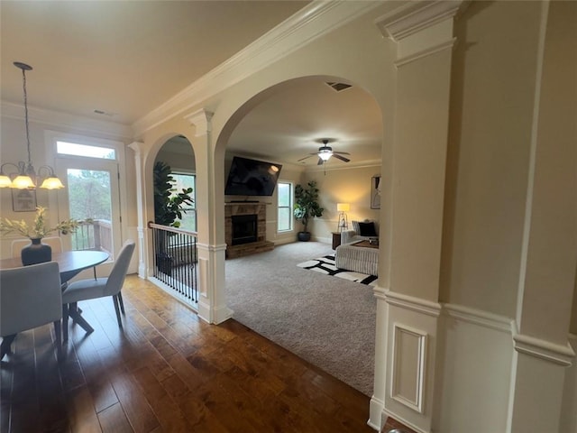 dining space with visible vents, crown molding, dark wood finished floors, a wainscoted wall, and a stone fireplace