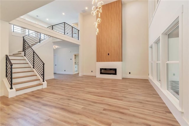 2808 S Arbor Dr, Gainesville, GA 30507 - unfurnished living room featuring a towering ceiling, stairs, light wood-style floors, a fireplace, and baseboards