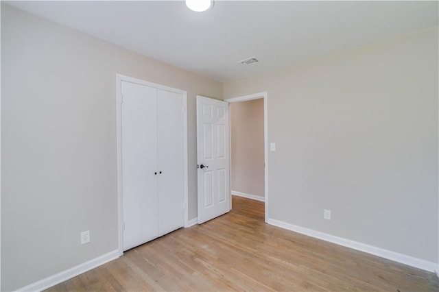 unfurnished bedroom with wood finished floors, a closet, visible vents, and baseboards
