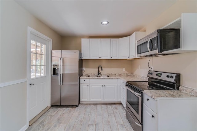 kitchen featuring light wood-type flooring, a sink, appliances with stainless steel finishes, and white cabinetry
