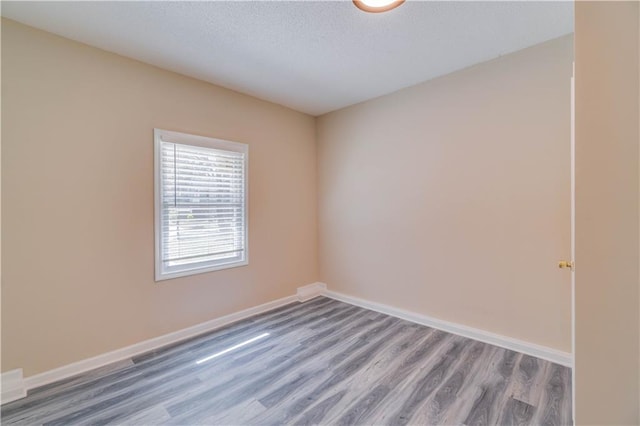 unfurnished room with a textured ceiling, wood finished floors, and baseboards