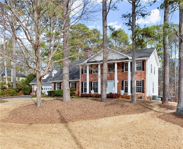 neoclassical home featuring an attached garage, a chimney, cooling unit, and brick siding