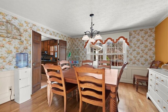 dining room featuring wallpapered walls, light wood-style flooring, a chandelier, and a wainscoted wall