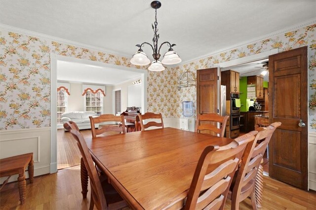 dining area featuring crown molding, wainscoting, light wood-style flooring, and wallpapered walls