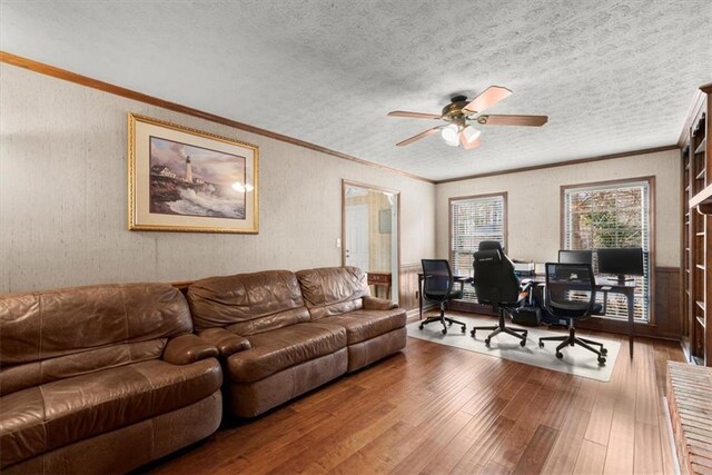 office area with a textured ceiling, a wainscoted wall, wood finished floors, a ceiling fan, and crown molding