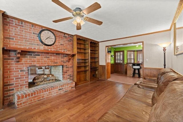 living area with a brick fireplace, ornamental molding, wood finished floors, and wainscoting
