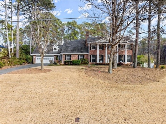 greek revival house featuring driveway, a garage, a chimney, and brick siding