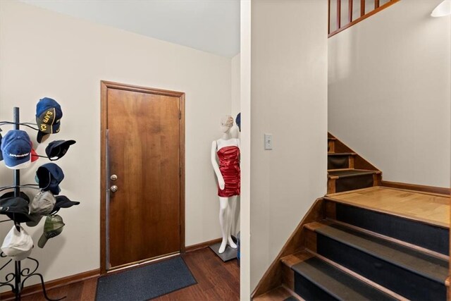 foyer entrance with dark wood finished floors, baseboards, and stairs