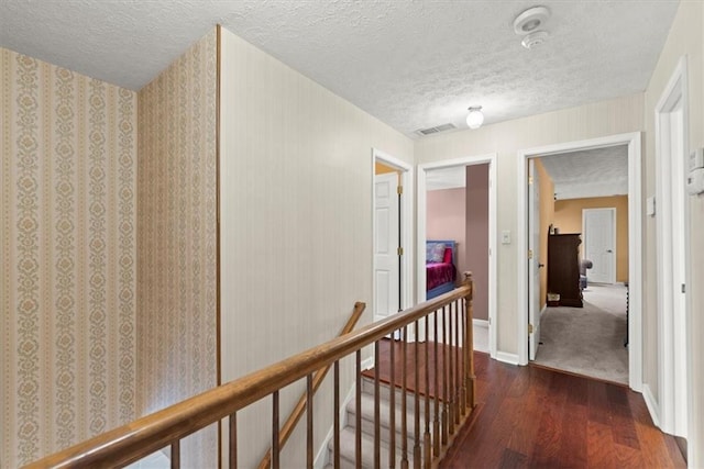 corridor featuring dark wood-style flooring, visible vents, a textured ceiling, an upstairs landing, and baseboards