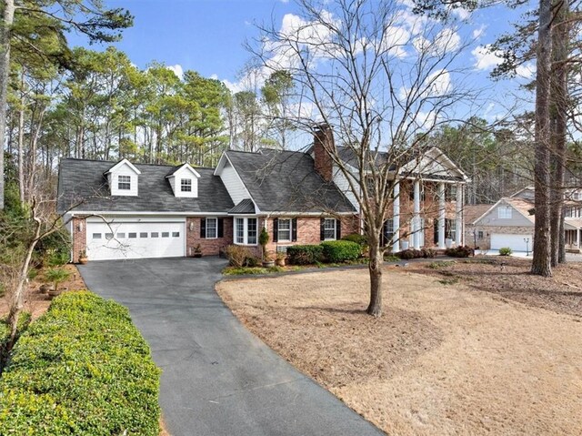 cape cod-style house featuring an attached garage, a chimney, aphalt driveway, and brick siding