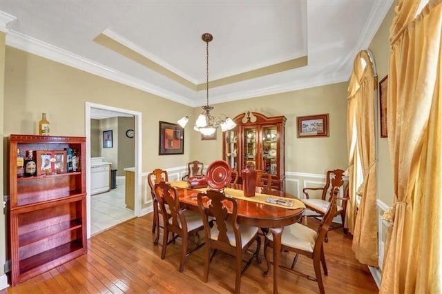 dining area with light wood-type flooring, a tray ceiling, a chandelier, and ornamental molding