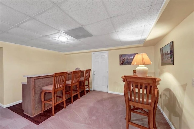 dining space with a drop ceiling, baseboards, carpet, and a dry bar