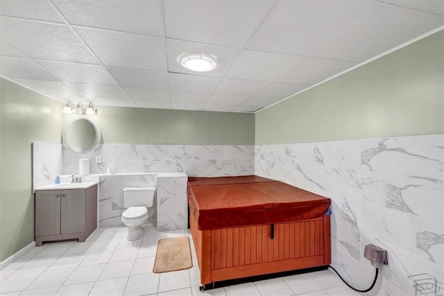 half bathroom with vanity, a drop ceiling, tile patterned flooring, tile walls, and toilet