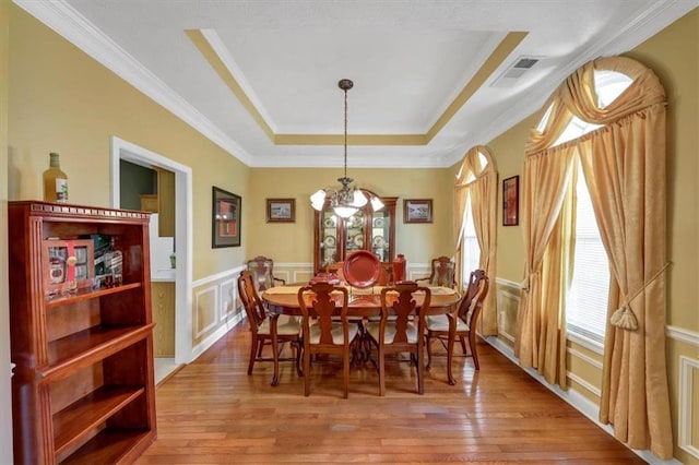 dining area featuring visible vents, hardwood / wood-style floors, an inviting chandelier, wainscoting, and a raised ceiling