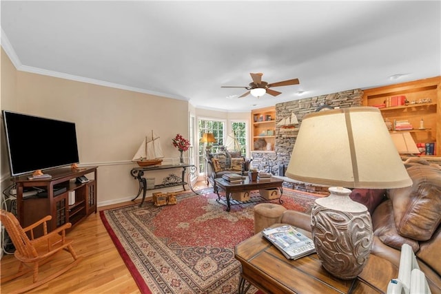 living room featuring built in shelves, ceiling fan, light wood-type flooring, and crown molding