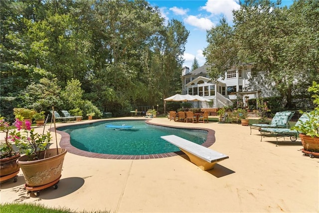 view of swimming pool featuring a patio area, a diving board, and a sunroom