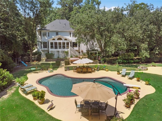 rear view of house featuring an outdoor fire pit, a patio area, a sunroom, a playground, and a lawn