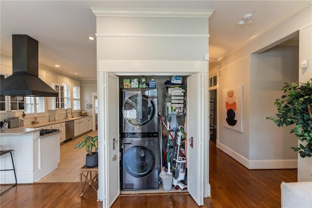 clothes washing area featuring sink, stacked washer / dryer, crown molding, and light wood-type flooring