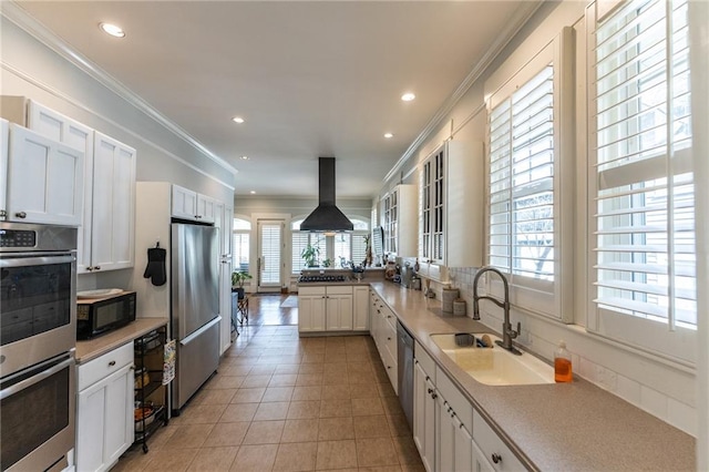 kitchen with white cabinetry, sink, island exhaust hood, appliances with stainless steel finishes, and kitchen peninsula