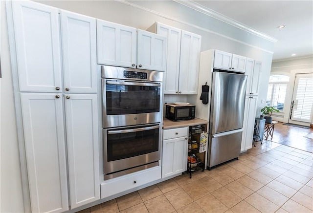 kitchen with white cabinetry, stainless steel appliances, ornamental molding, and light tile patterned floors