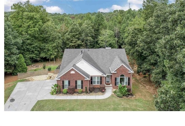 view of front of property with a forest view, brick siding, and a front lawn