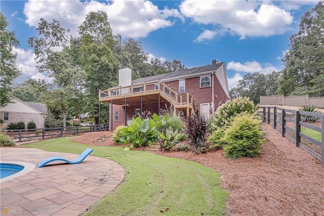 back of property with brick siding, a yard, a chimney, a deck, and a fenced backyard