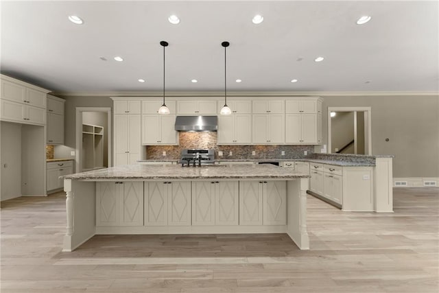 kitchen with under cabinet range hood, a peninsula, ornamental molding, and backsplash