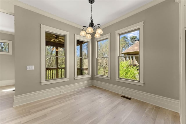 unfurnished dining area featuring visible vents, ornamental molding, an inviting chandelier, baseboards, and light wood-style flooring