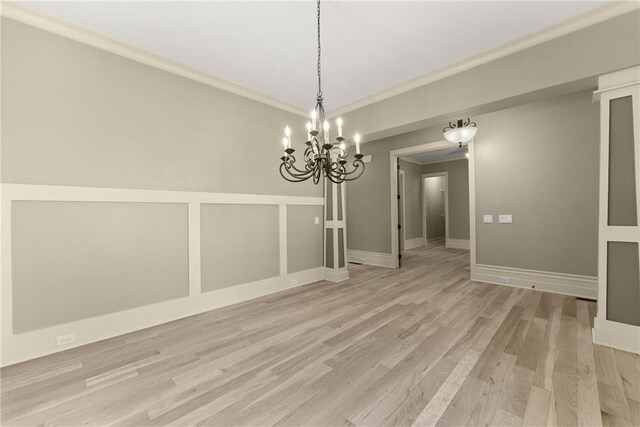 unfurnished dining area with light wood-style floors, baseboards, ornamental molding, and a notable chandelier