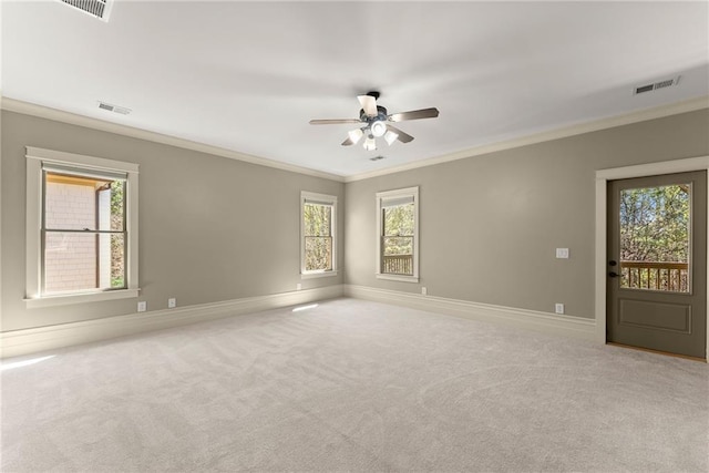 carpeted empty room featuring crown molding, a wealth of natural light, ceiling fan, and visible vents