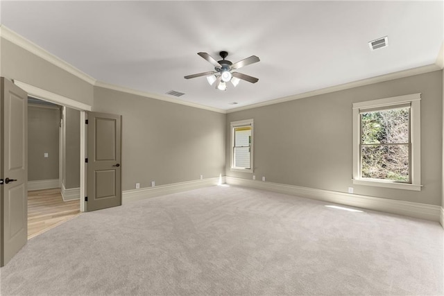 empty room with ceiling fan, light colored carpet, visible vents, baseboards, and ornamental molding